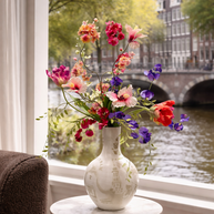 Vaas met Amsterdamgrafitti gespote met kleurrijke zijden bloemen erin. De grachten van Amsterdam op de achtergrond